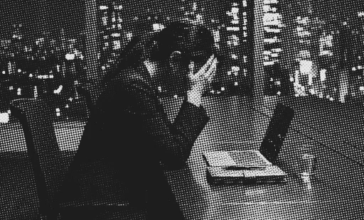 夜のオフィスでノートPCを前に頭を抱える担当者