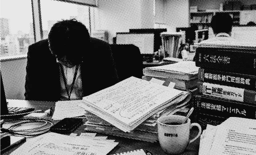 資料や書類が山積みになったデスクで作業する編集者